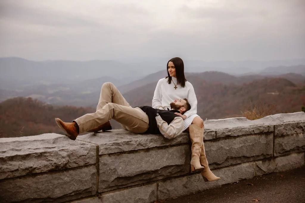 Couple relaxing on Foothills Parkway overlook wall with mountain views, showcasing casual engagement photos clothes styled by Gatlinburg photographer during fall engagement session