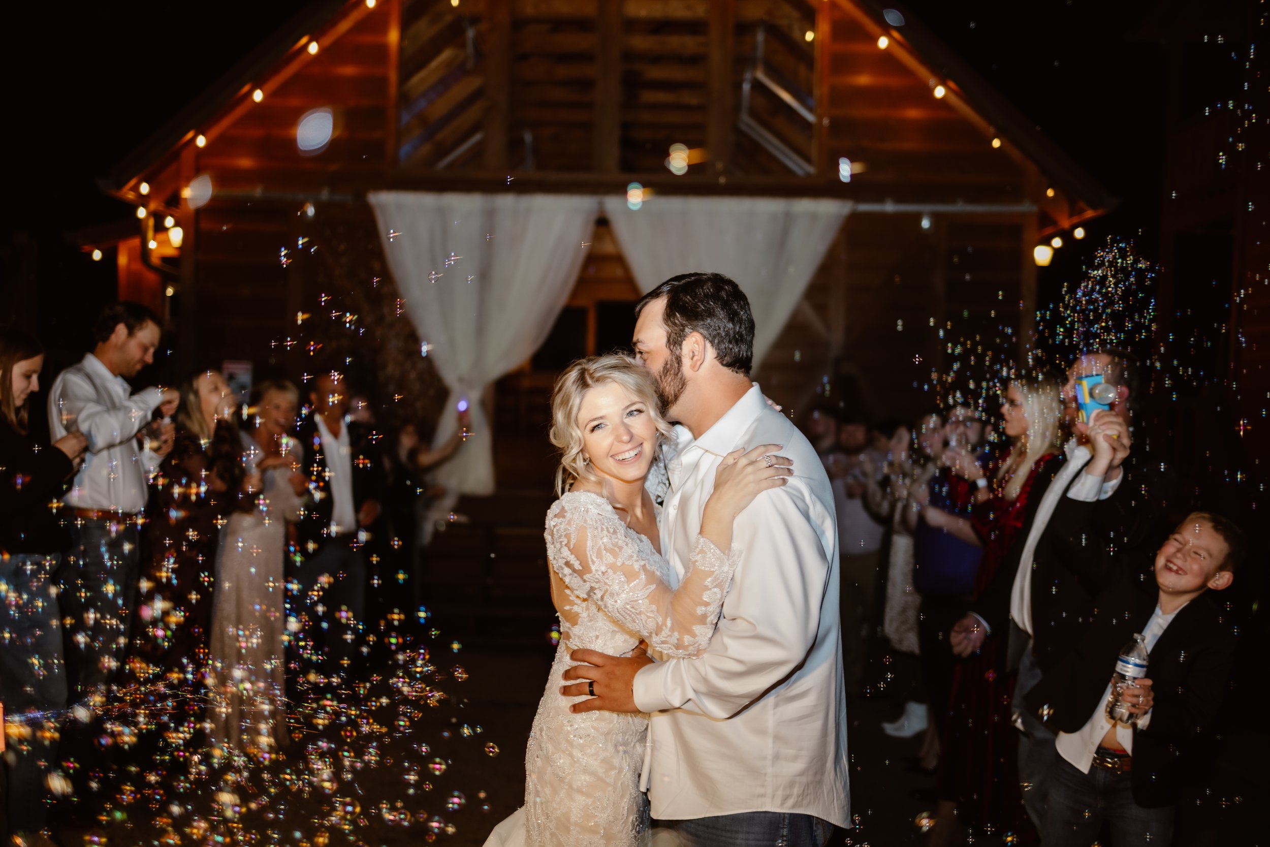 Bride and groom sharing a romantic nighttime dance surrounded by glowing bubbles and wedding guests outside the rustic cabin venue at Parkside resort.