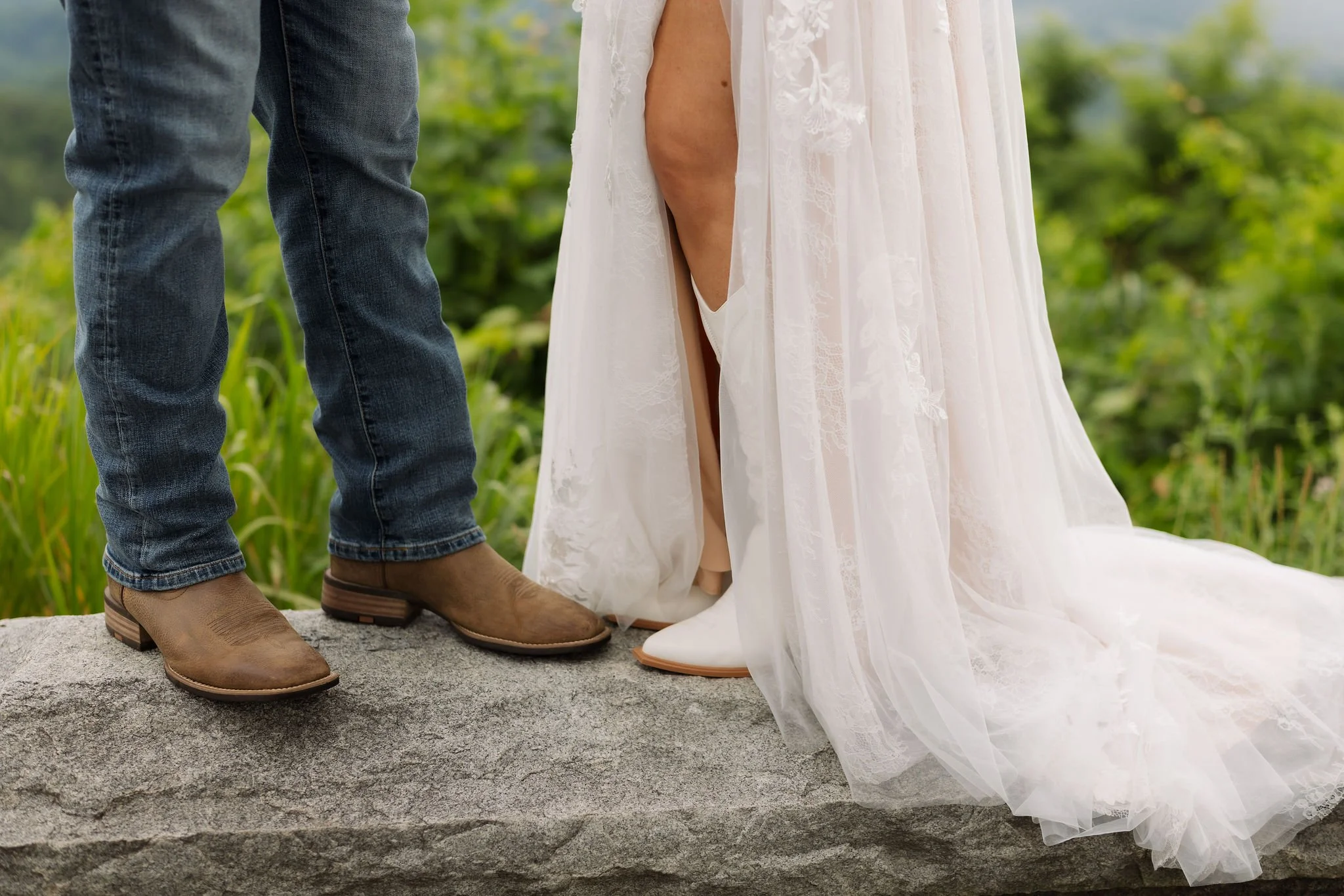 Close-up of the bride's white cowboy boots beneath her flowing lace wedding dress beside the groom's brown boots and jeans during their Gatlinburg elopement.