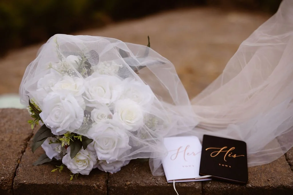 Bridal bouquet, veil, and vow books arranged on a stone ledge at Gatlinburg wedding cabins, styled and photographed by an elopement photographer with mountain scenery nearby.