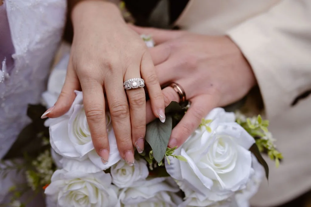Wedding rings displayed on the bride and groom’s hands resting on a white rose bouquet during an intimate ceremony at Gatlinburg wedding cabins, photographed by an elopement photographer.