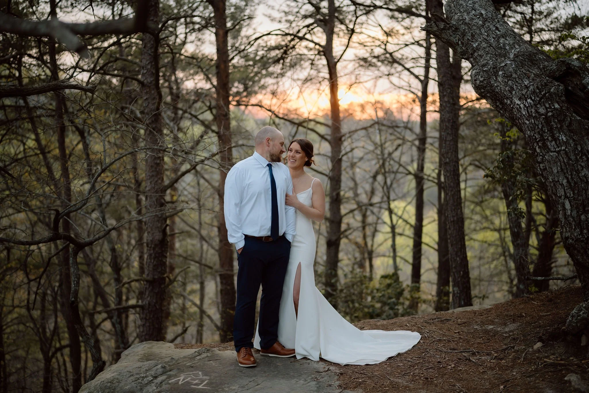 Bride and groom stand together among tall trees at sunset, captured by their gatlinburg photographer after their outdoor elopement.