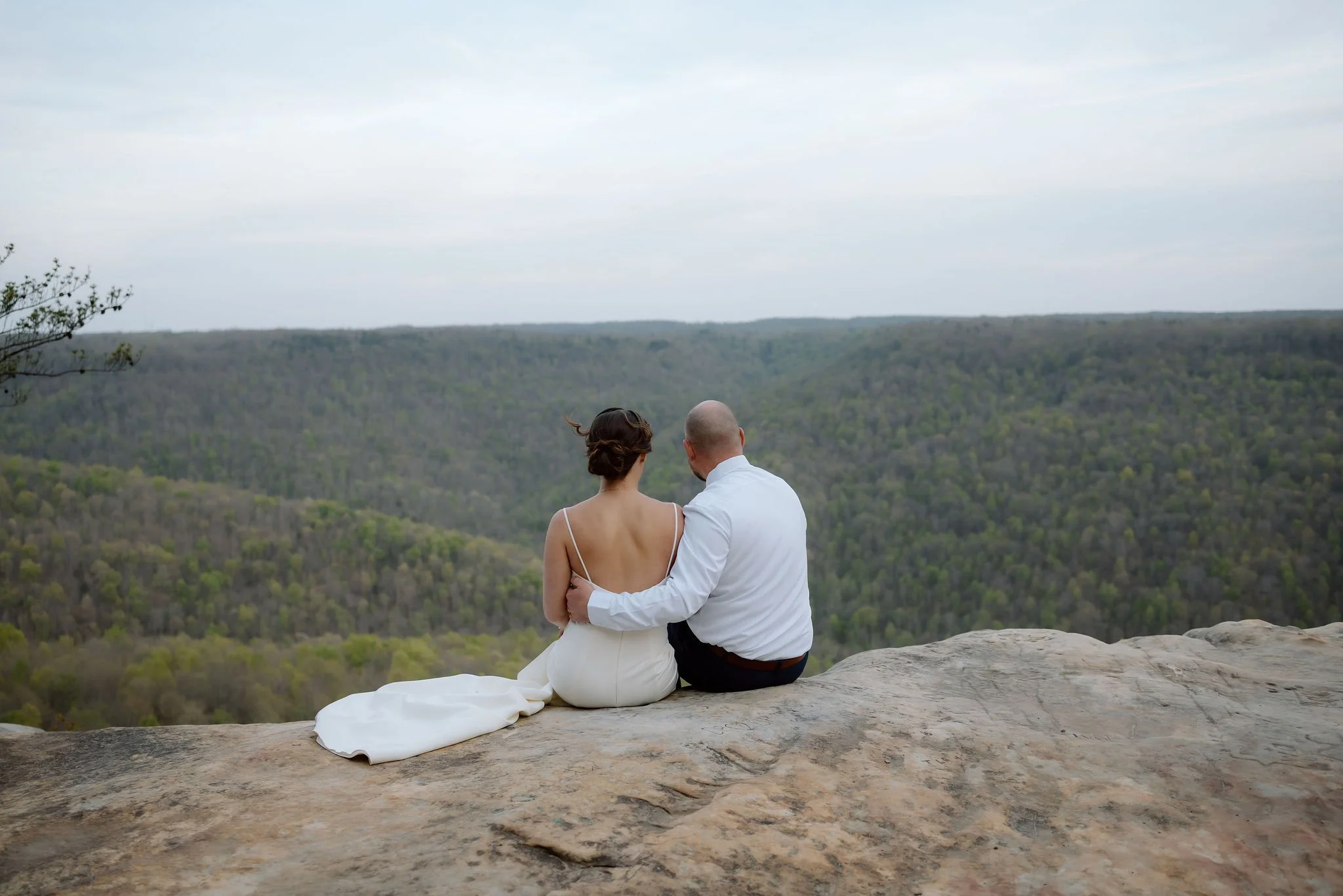 Newlyweds sit together on the rocky edge of bee rock overlook, photographed by their gatlinburg photographer against sweeping mountain views.