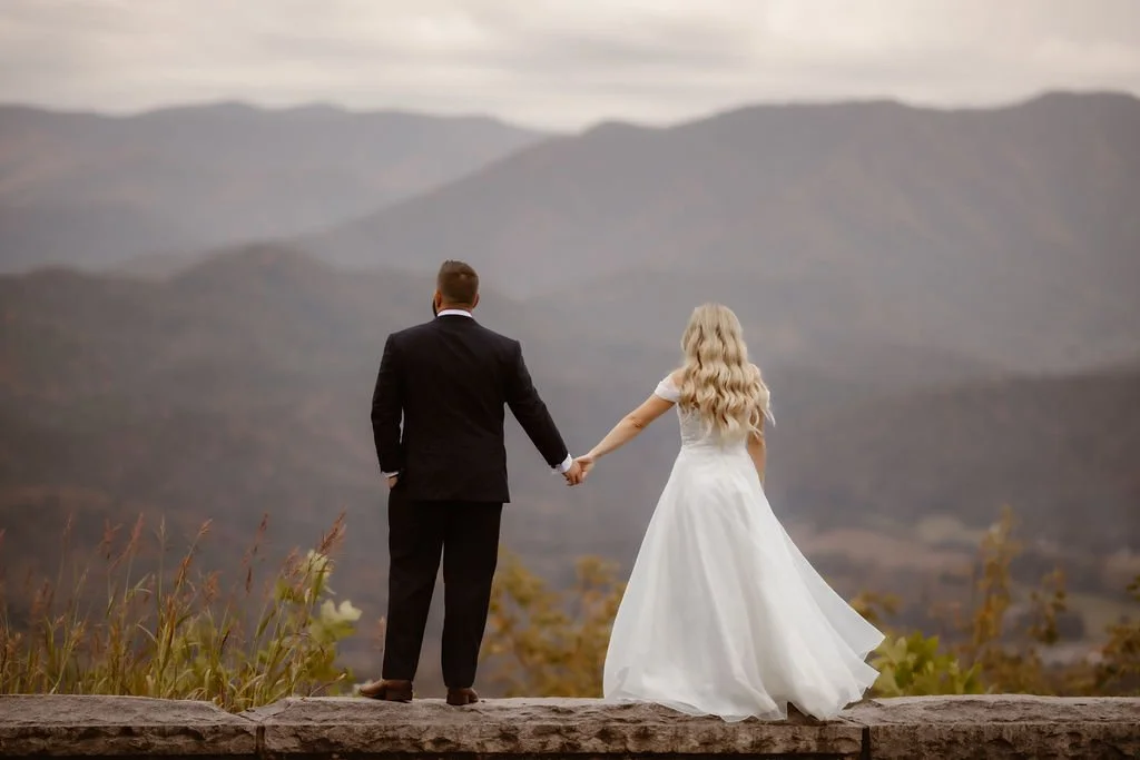 Bride and groom stand hand in hand with their backs to the camera, overlooking the Smoky Mountains during their Foothills Parkway micro wedding in Gatlinburg.
