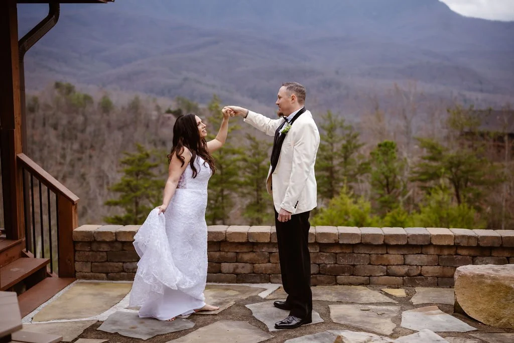 Bride twirling beneath the groom’s raised hand on a stone patio overlooking the mountains during wedding portraits.