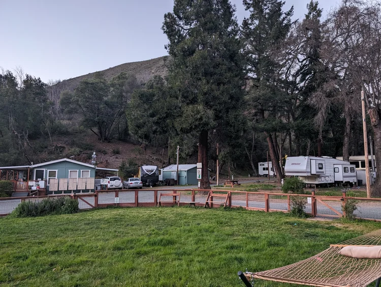 RV park with several trailers and a small building in a wooded area, grassy foreground