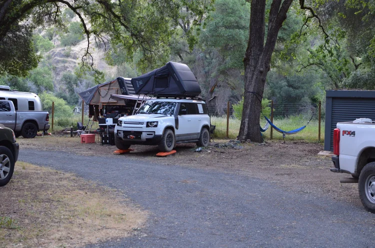 Campsite with a white SUV featuring a rooftop tent, parked next to a tree