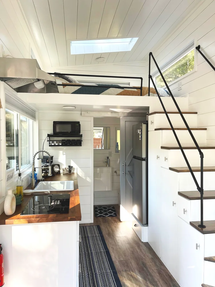 Interior of a tiny house with a loft bed, kitchen, and bathroom