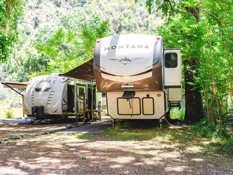 Two RVs parked in a shaded campsite surrounded by trees