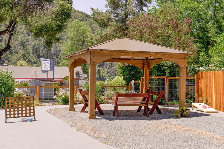 Outdoor picnic area with wooden gazebo, benches, and lawn games like cornhole and Connect Four in a park setting