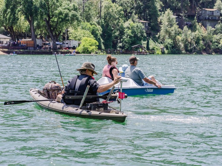 People kayaking and pedaling a boat on a lake surrounded by trees and houses