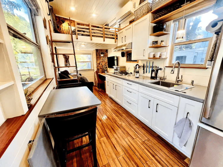 Interior of a modern tiny house with wooden floors, white cabinets, and a loft bed