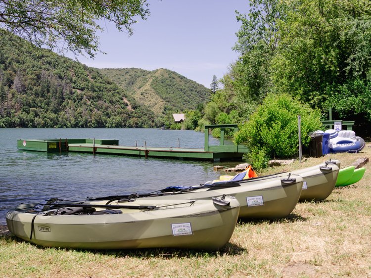 Kayaks and an inflatable boat by a lake dock with forested hills in the background