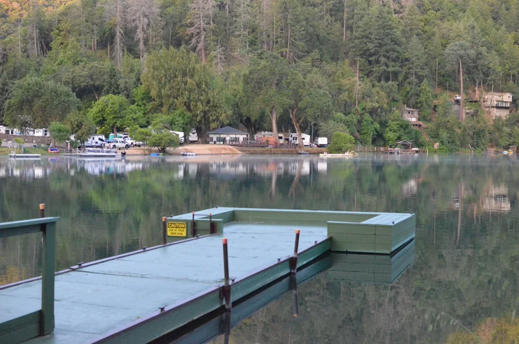 A tranquil lakeside scene featuring a green wooden dock extending over calm water in the foreground