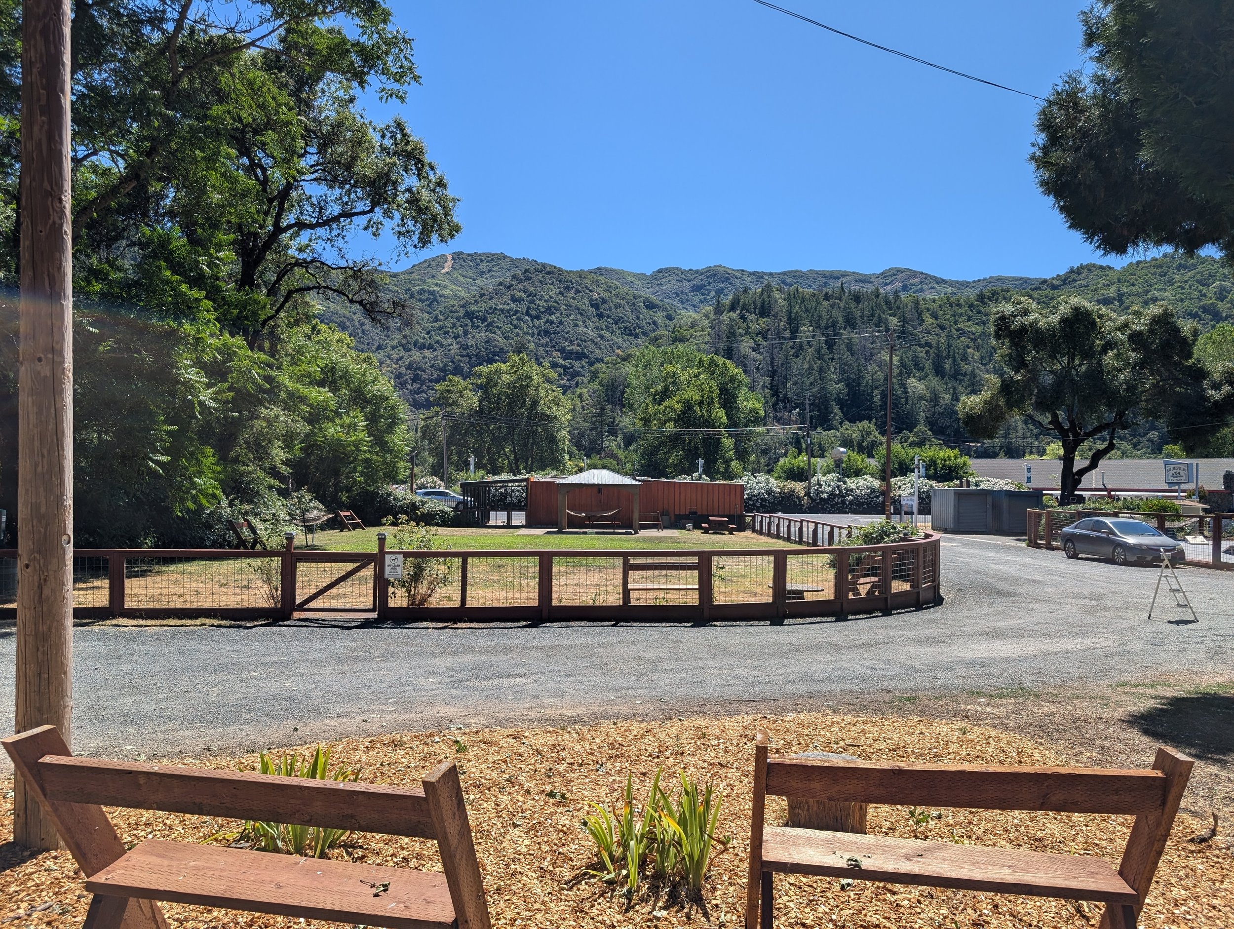 Outdoor scene with a wooden fence, benches, and a hill in the background under a clear blue sky.
