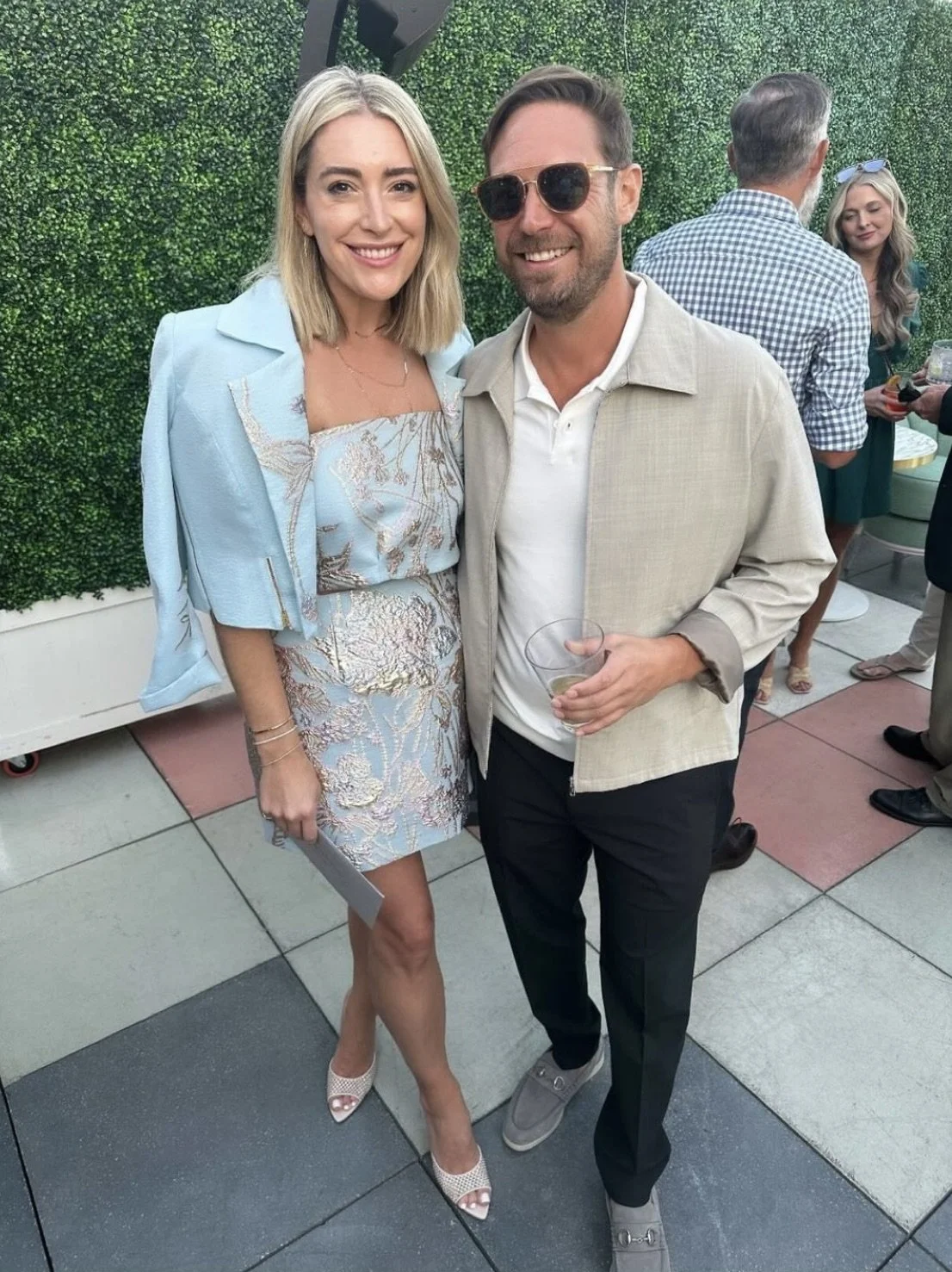 Woman wearing a custom three-piece ensemble with a baby blue organza jacket featuring leaf accents, paired with a floral metallic tube top and matching mini A-line skirt at a nighttime rooftop rehearsal dinner.