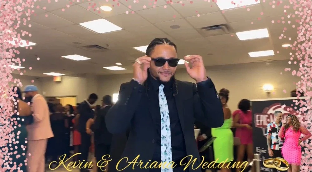 Man wearing a black suit, black shirt, and floral tie, adjusting sunglasses at a wedding reception, with a pink, black, and white floral border, and text indicating it is Kevin and Ariana's wedding.