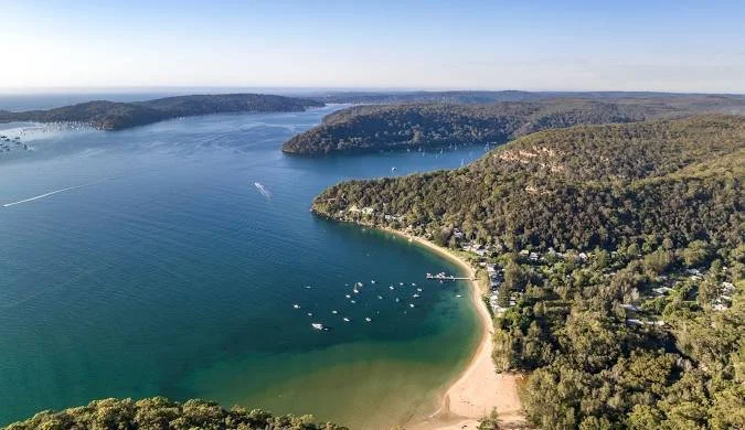 Aerial view of a large body of water with boats, surrounded by green forested hills and a small beach.