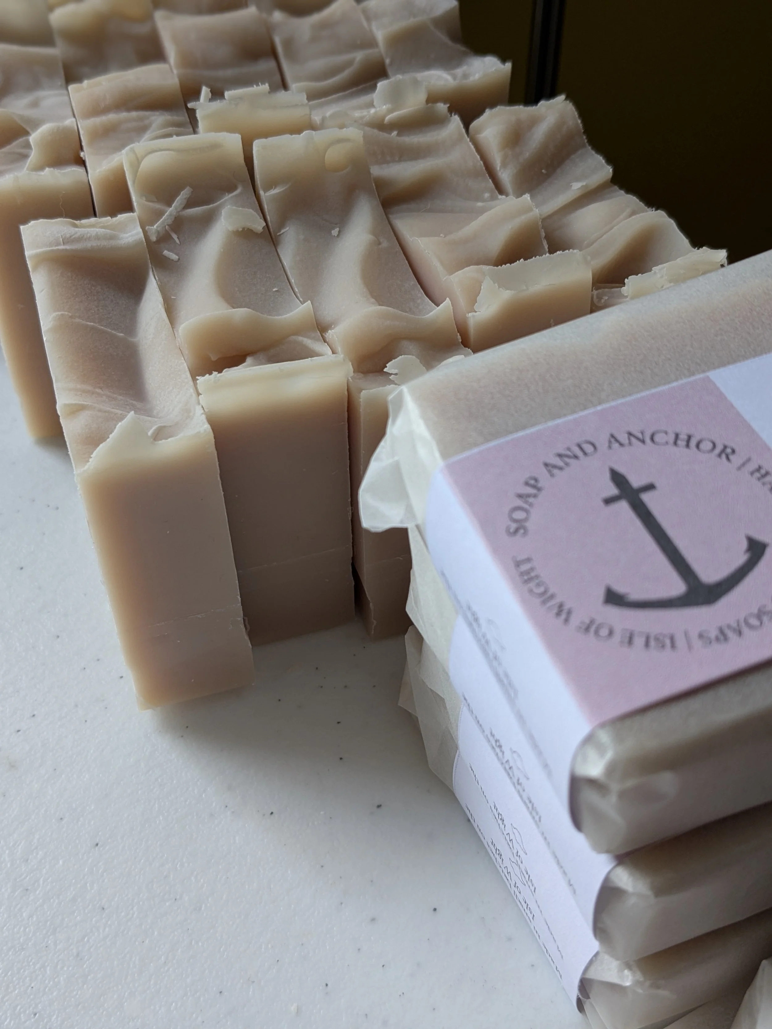 A stack of homemade soap bars with a white label featuring a black anchor logo and text on white paper wrapping.