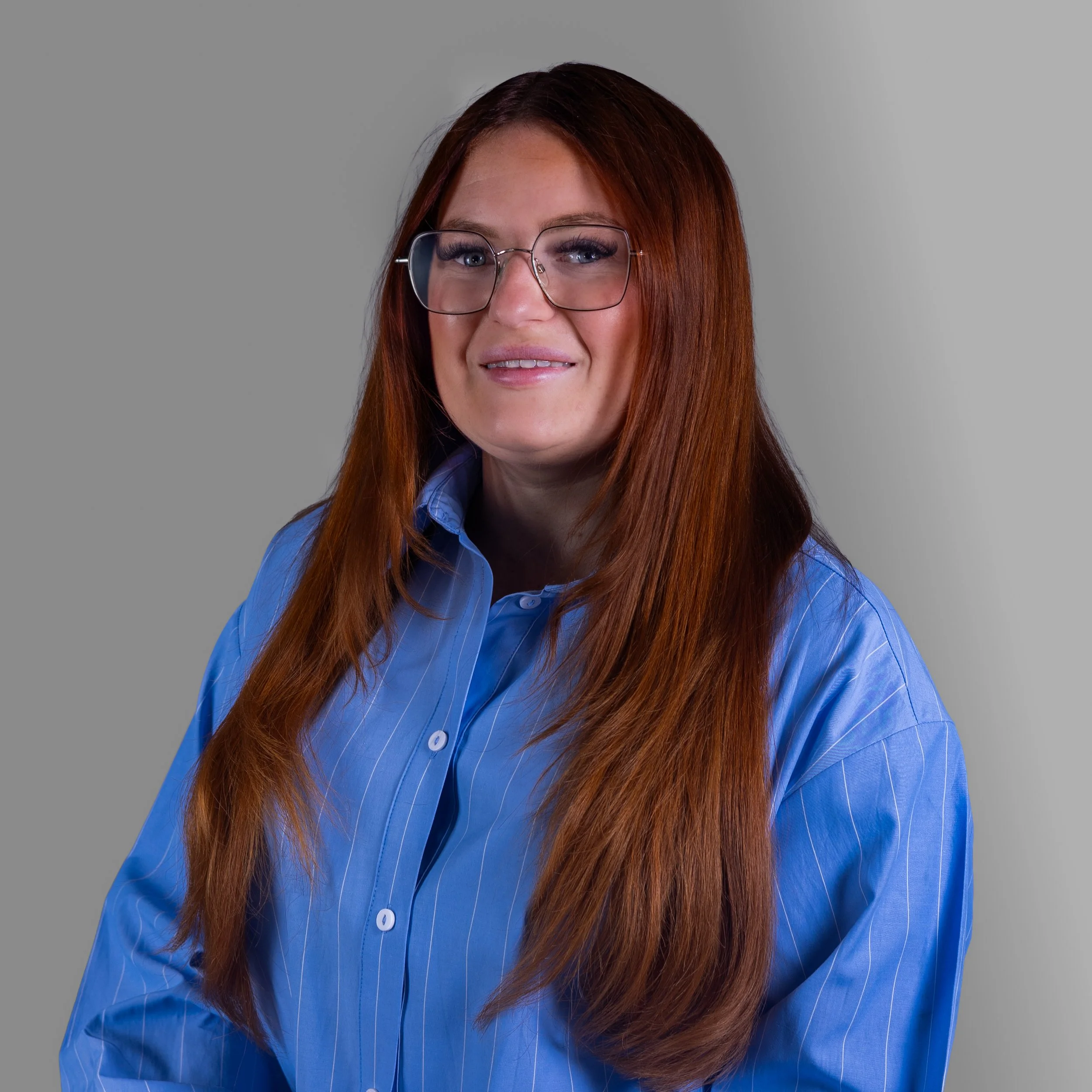 Person with long hair and glasses wearing a black turtleneck, standing against a brick wall.