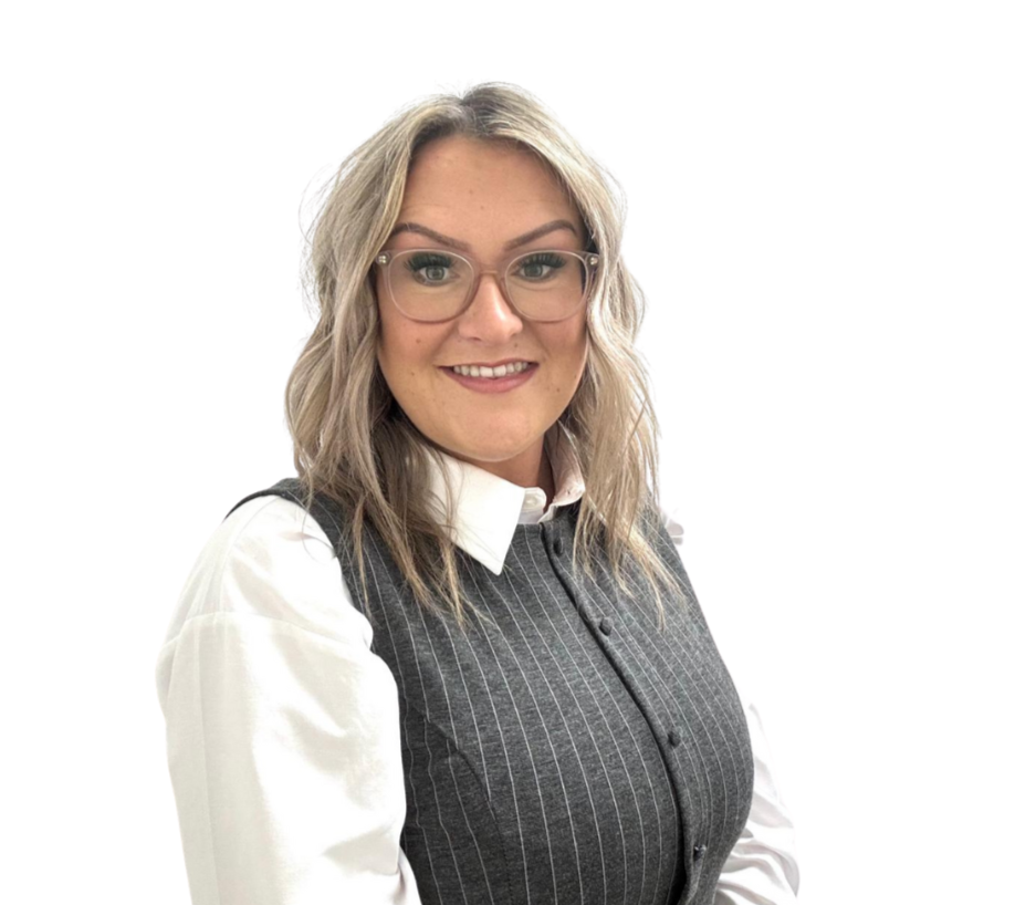 Woman with glasses and floral dress sitting in front of a brick wall.