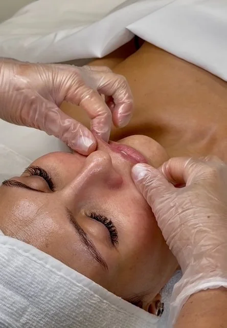 A woman receives a waxing treatment on her upper lip by a professional wearing gloves in a clinic room.