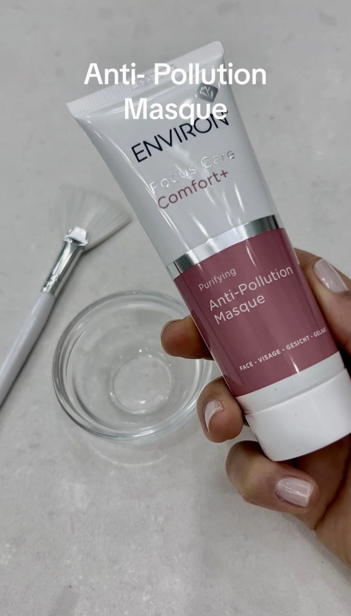 Person holding a tube of Environ Purifying Anti-Pollution Masque with a white brush and a glass bowl nearby.
