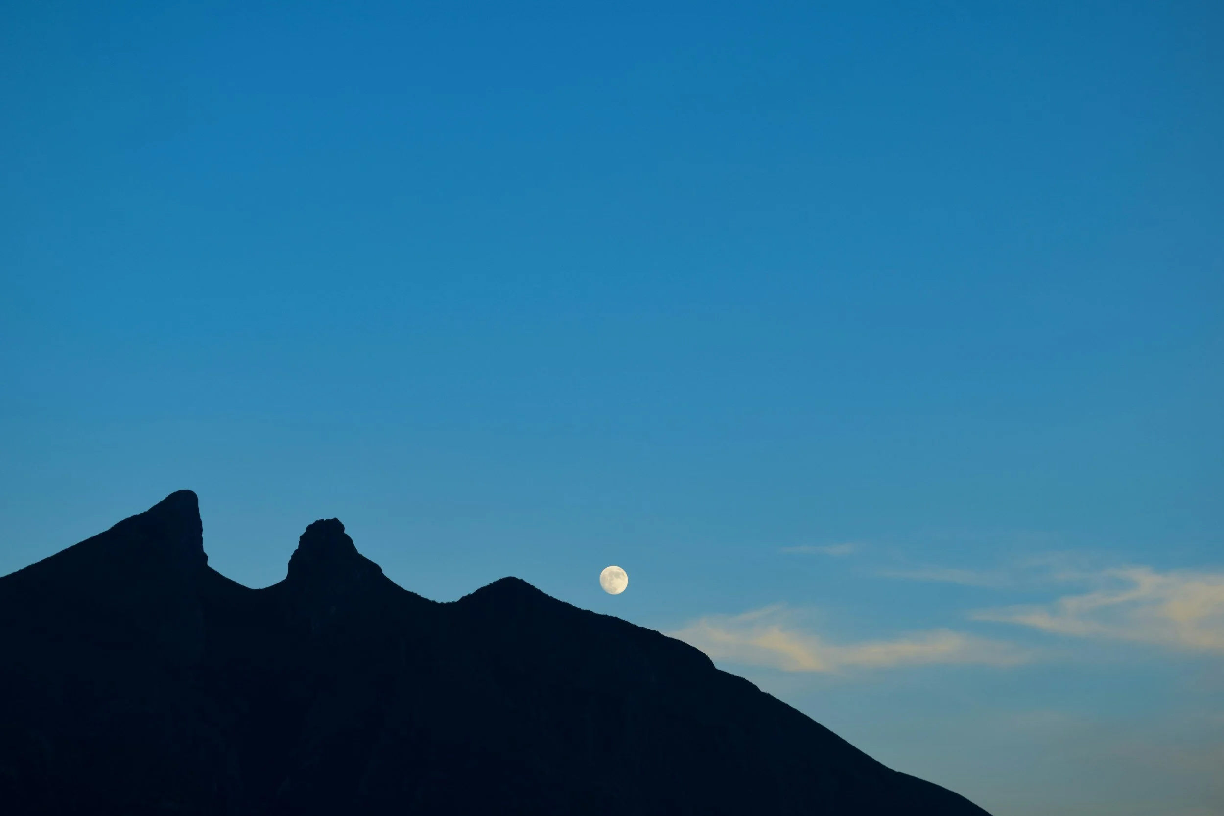 Silhouetted mountain peaks in Monterrey Cerro de la Silla with a full moon in a clear blue sky