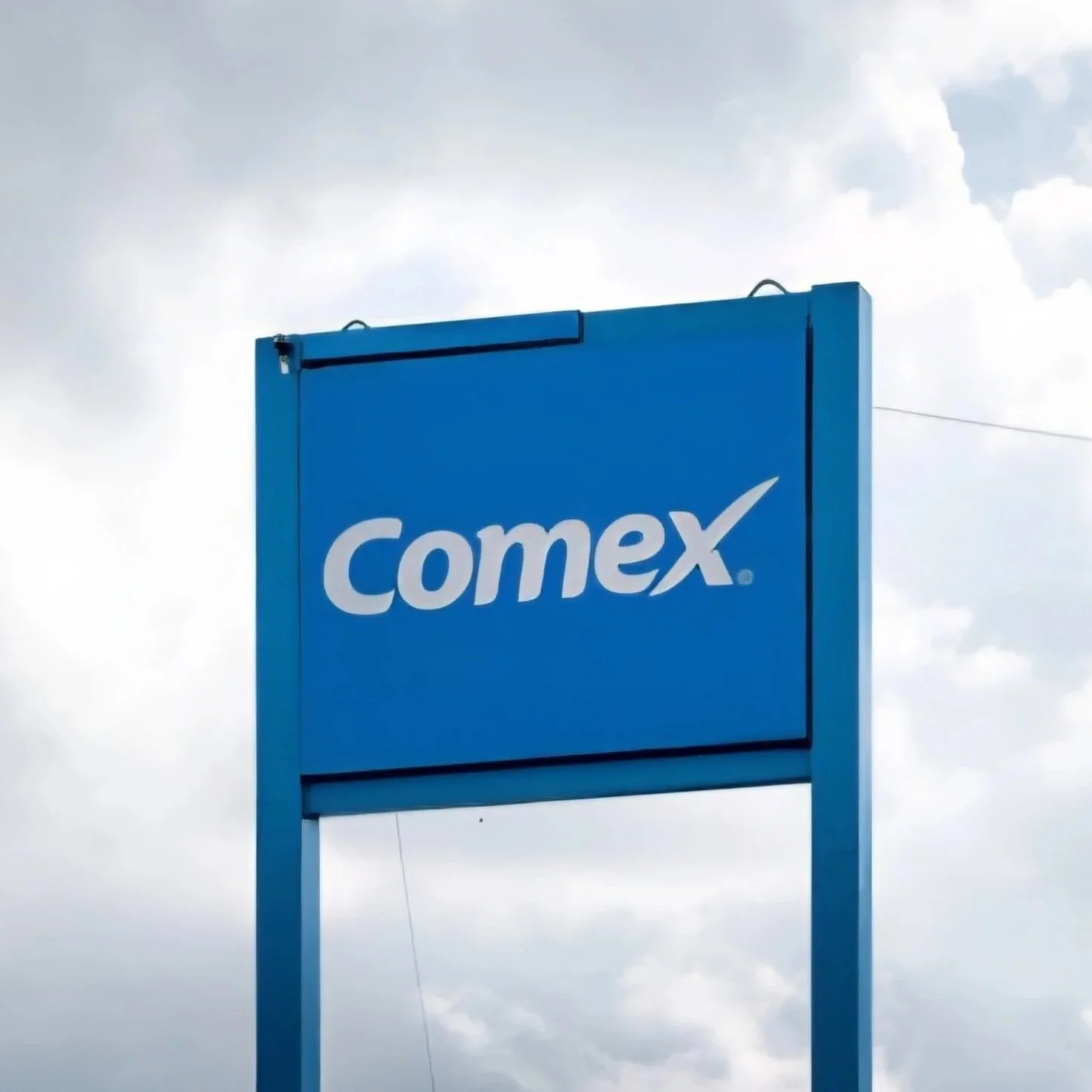 Blue sign with white 'comex' logo against cloudy sky background.