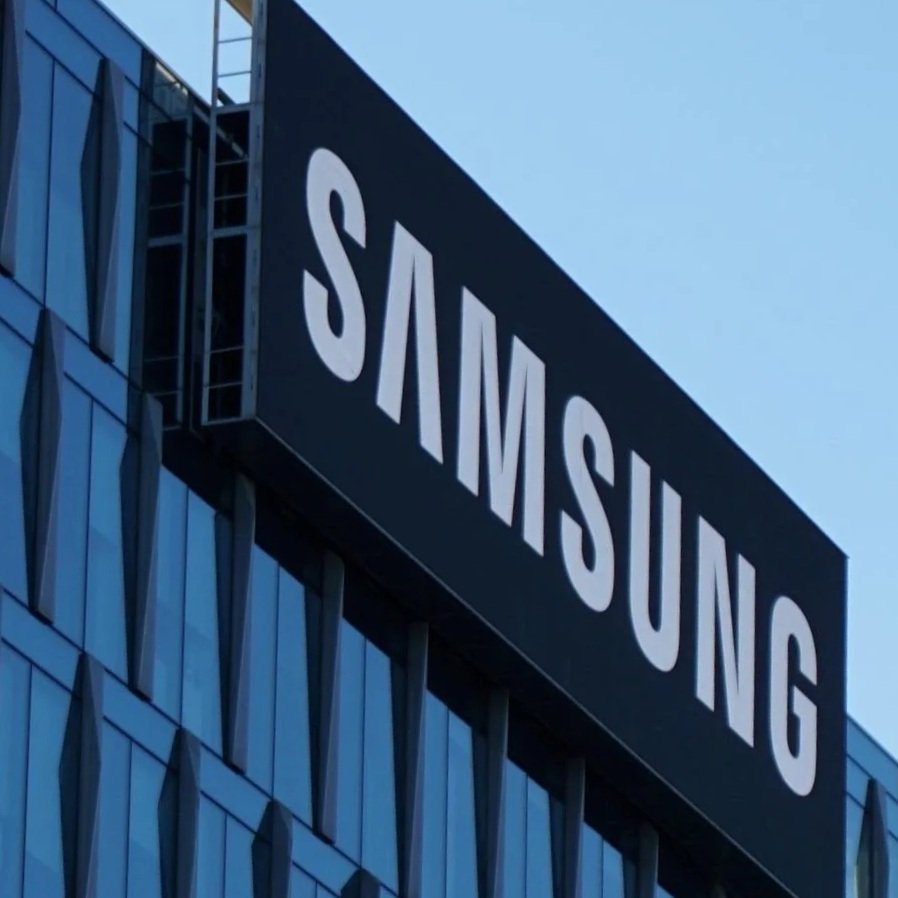 Close-up of a building with blue glass windows and a large black sign with the white Samsung logo on it.