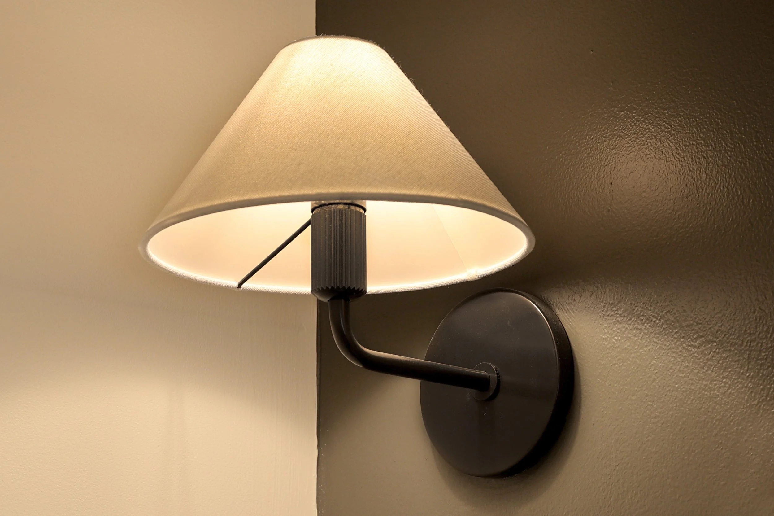 Wall-mounted lamp with a beige fabric shade on a light-colored wall.