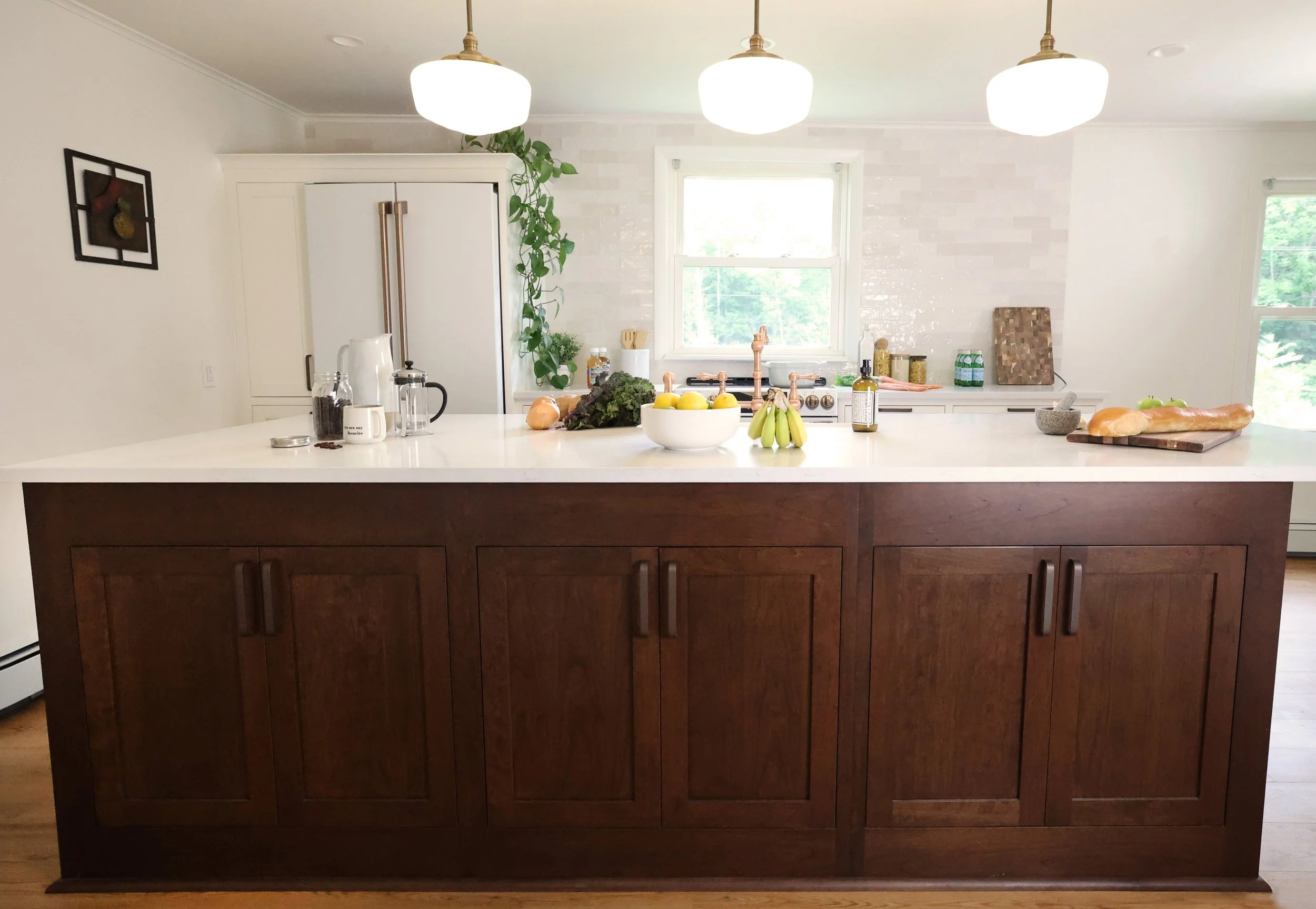 Modern kitchen with white island countertop, wooden cabinets, pendant lighting, window, various foods, and kitchen essentials.