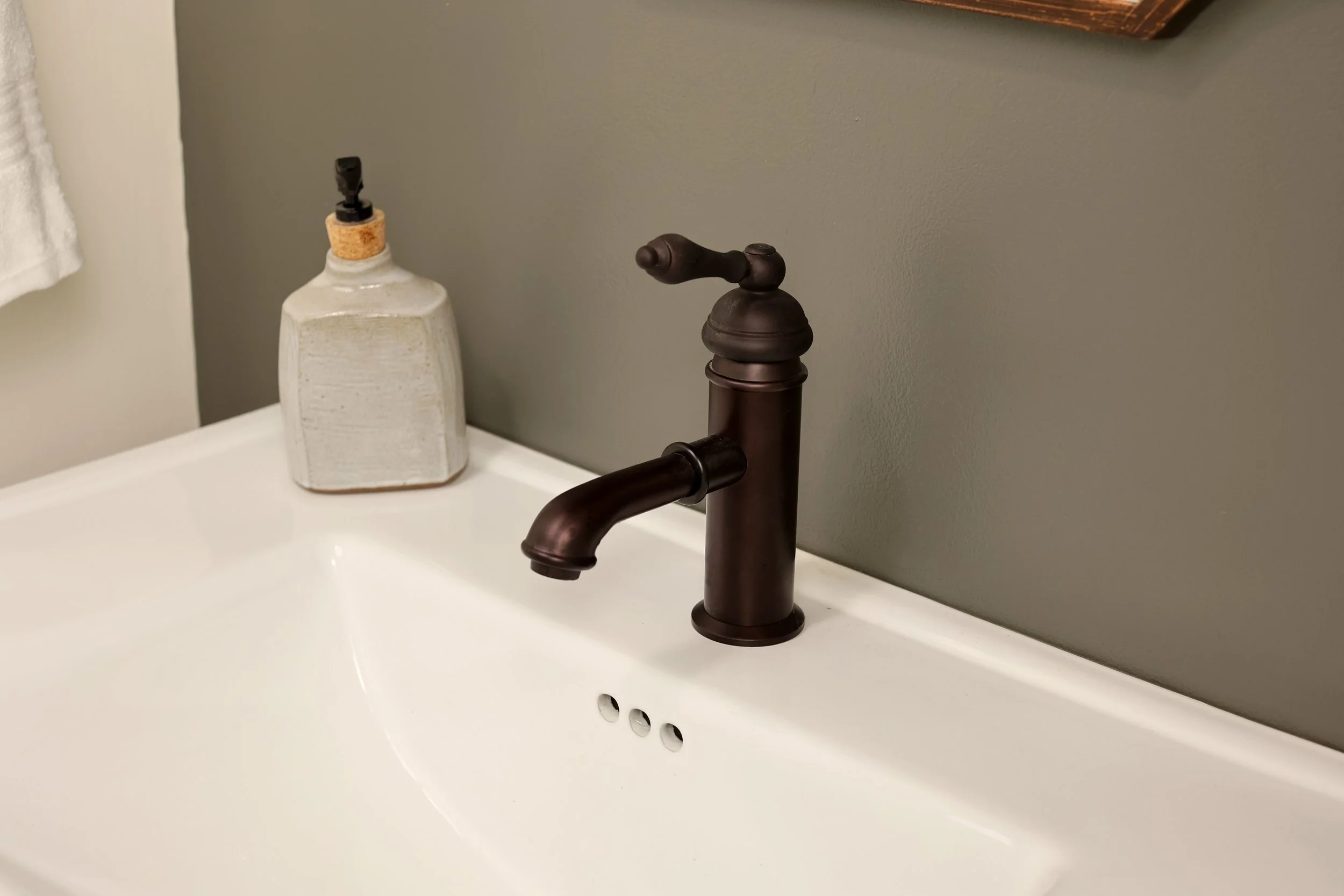 Bathroom sink with bronze faucet and a soap dispenser on the side.