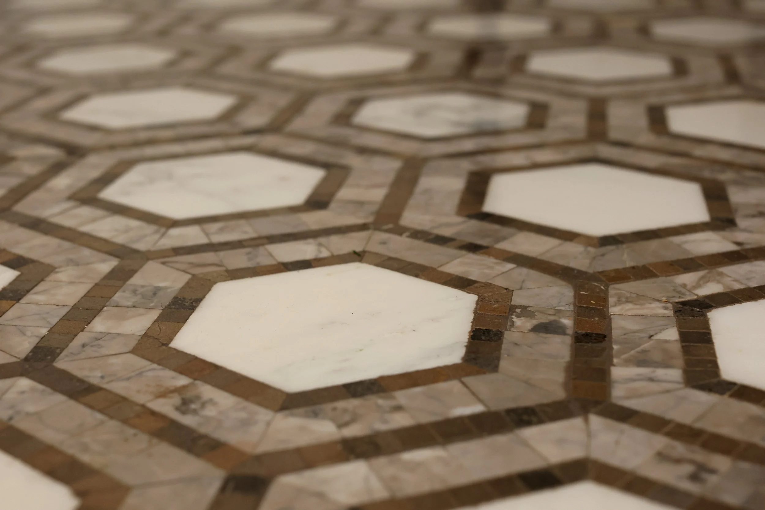 Close-up of a geometric patterned tiled floor with hexagon and square shapes in shades of white, gray, and brown.