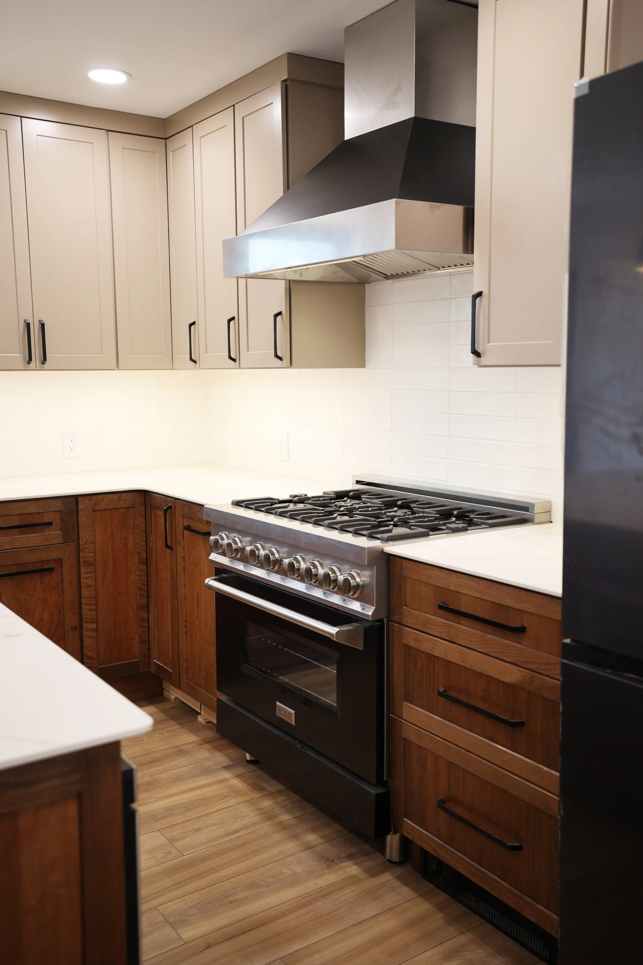 Modern kitchen with beige and wooden cabinets, stainless steel range hood and oven, gas stove, white backsplash, and wood flooring.