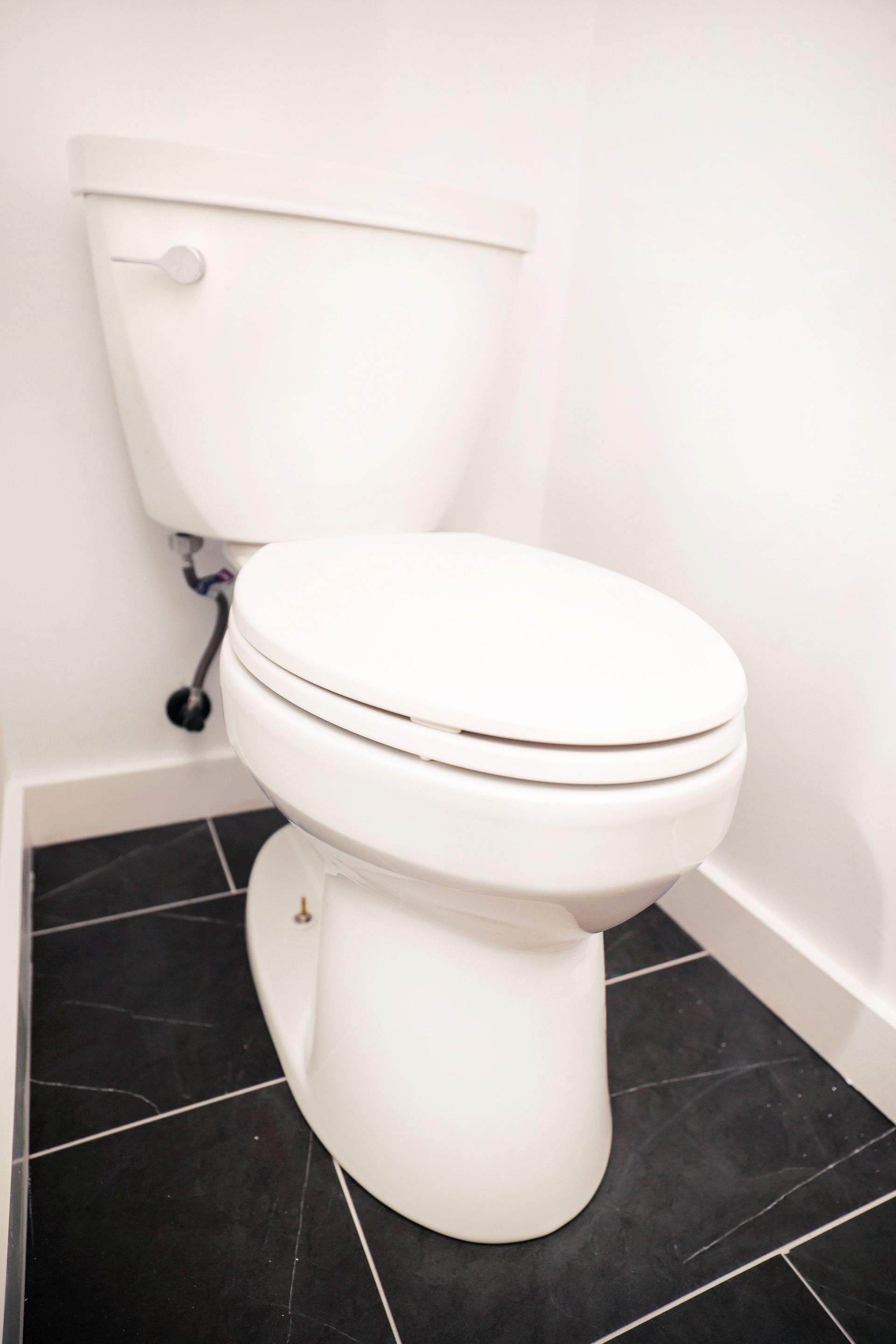 White toilet with closed lid in a bathroom with black tiled floor and white walls.