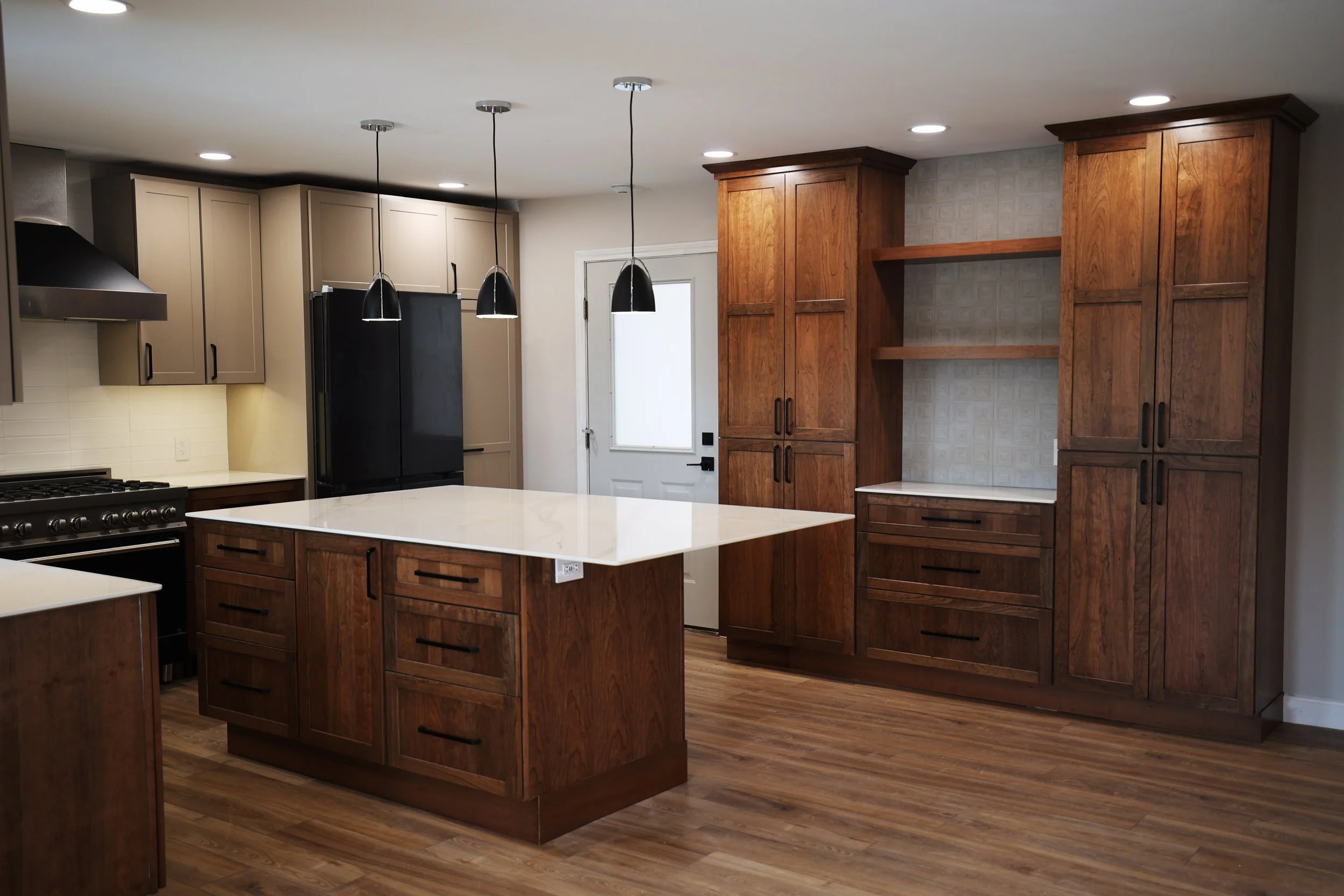 Modern kitchen with wooden cabinets, white countertops, black refrigerator, and black pendant lights hanging above the central island.