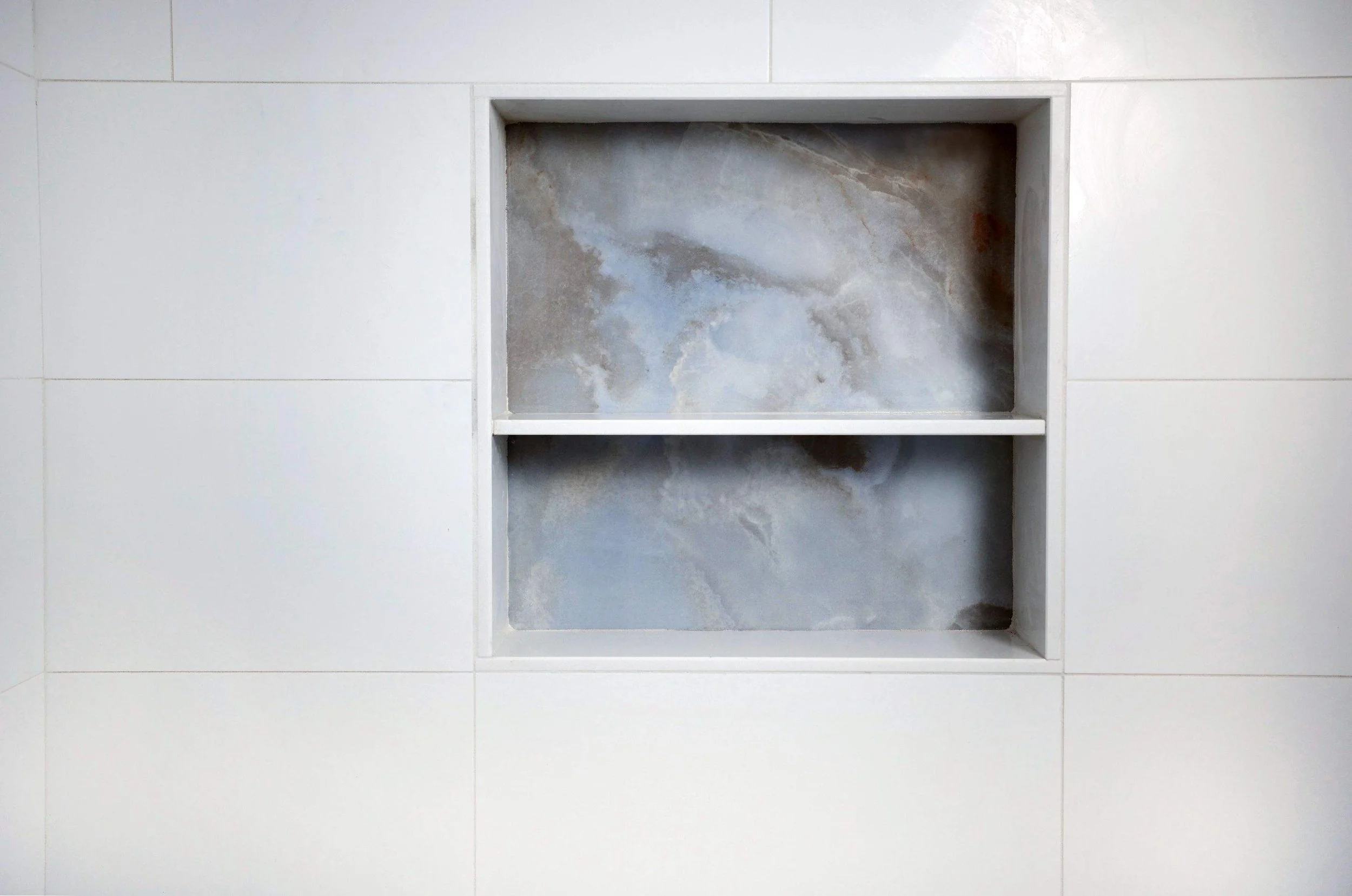 A built-in wall niche with a marble back inside a bathroom wall with white tiles.