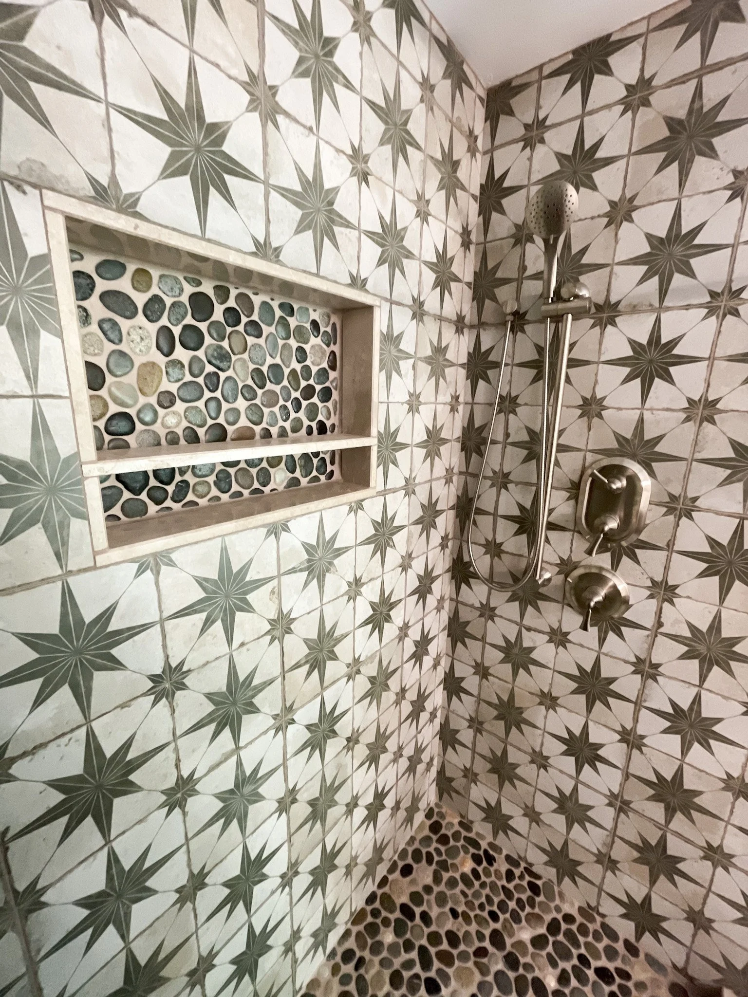 Shower area with patterned star and circle tiles, pebble-floor shower and built-in pebble niche.