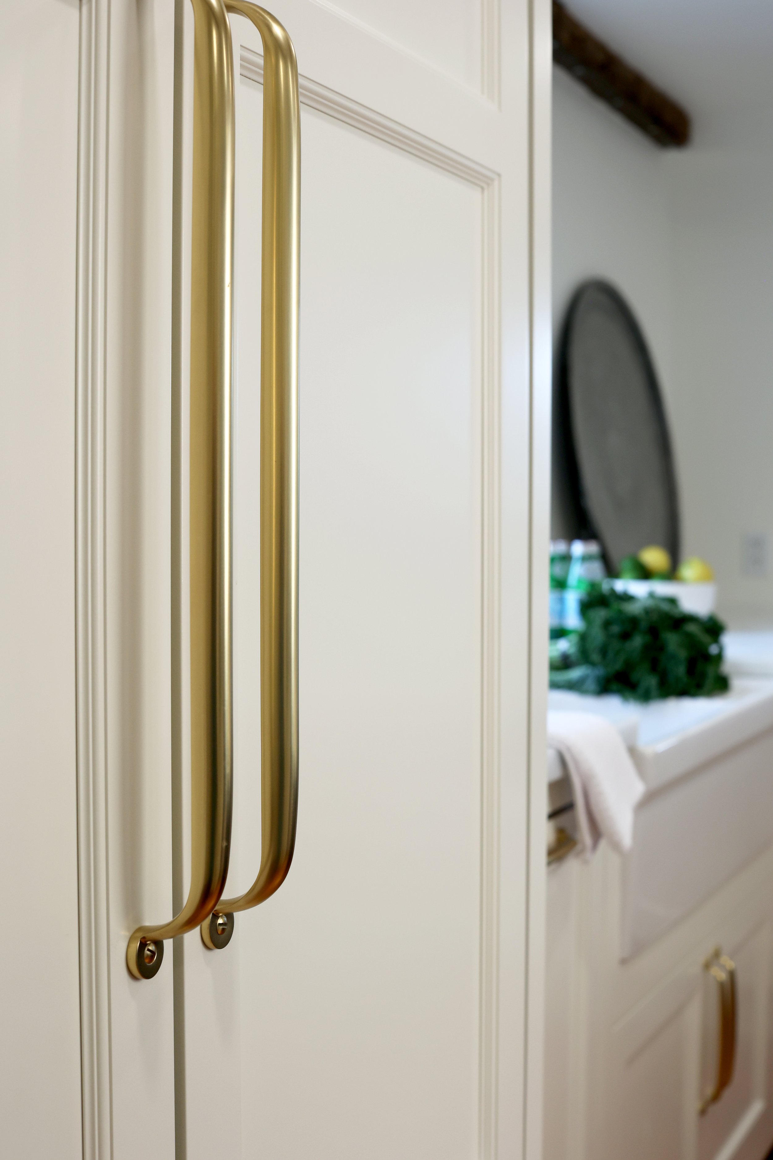 Elegant kitchen featuring panel ready sub zero refrigerator with brass hardware, custom white cabinetry, and restored original beams in a historic Upper Valley home. 