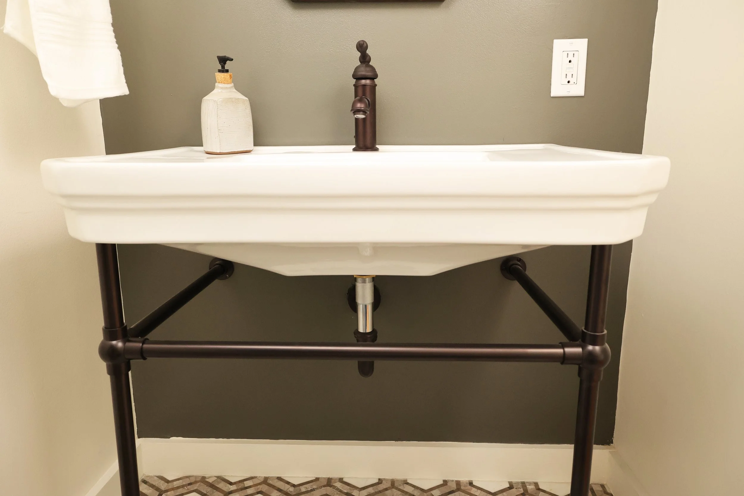 Bathroom vanity with a white sink, a bronze faucet, a soap dispenser, and a towel, against a dark gray wall.