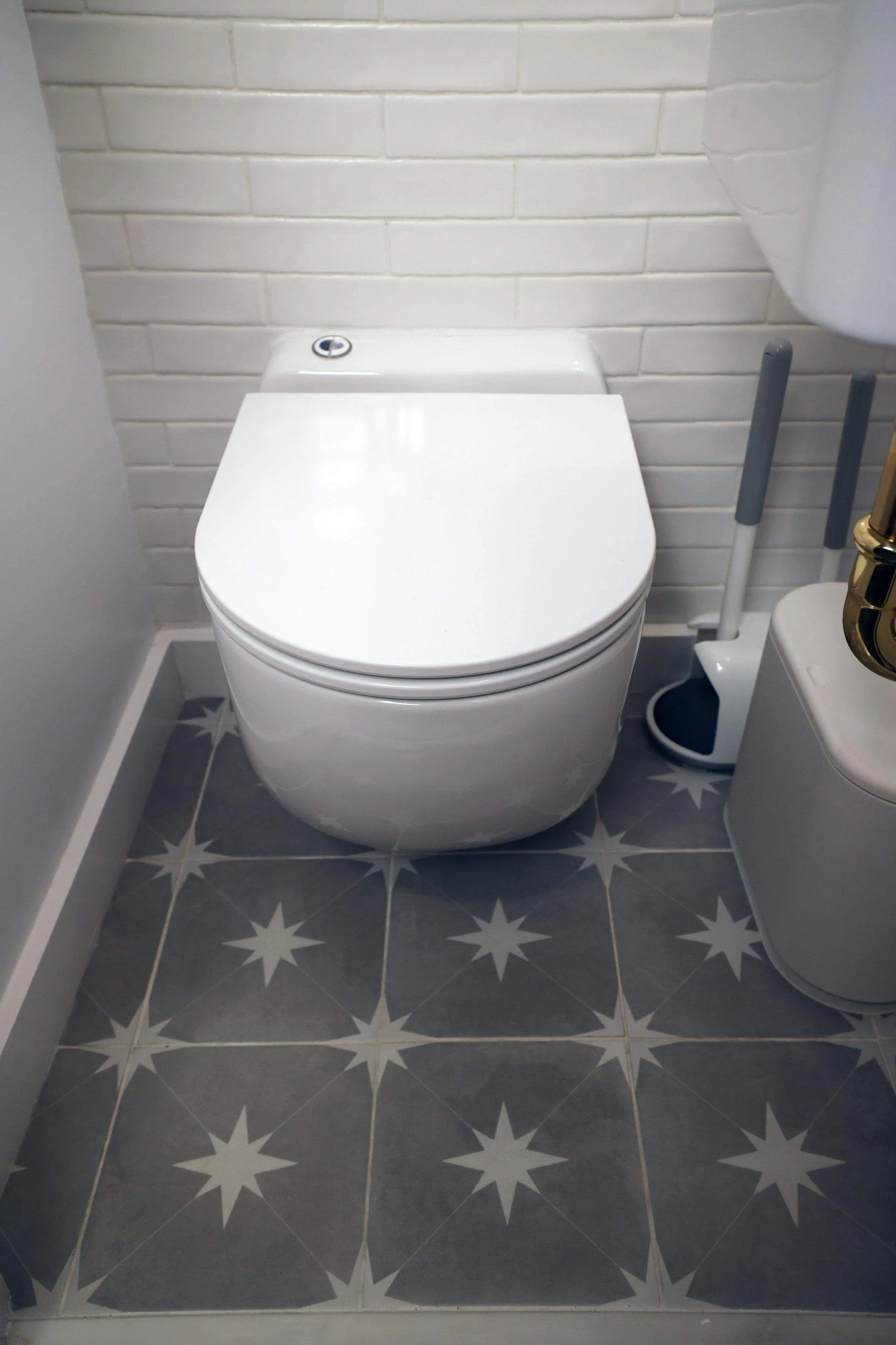 Modern white toilet in a bathroom with patterned tile flooring and a white brick wall.