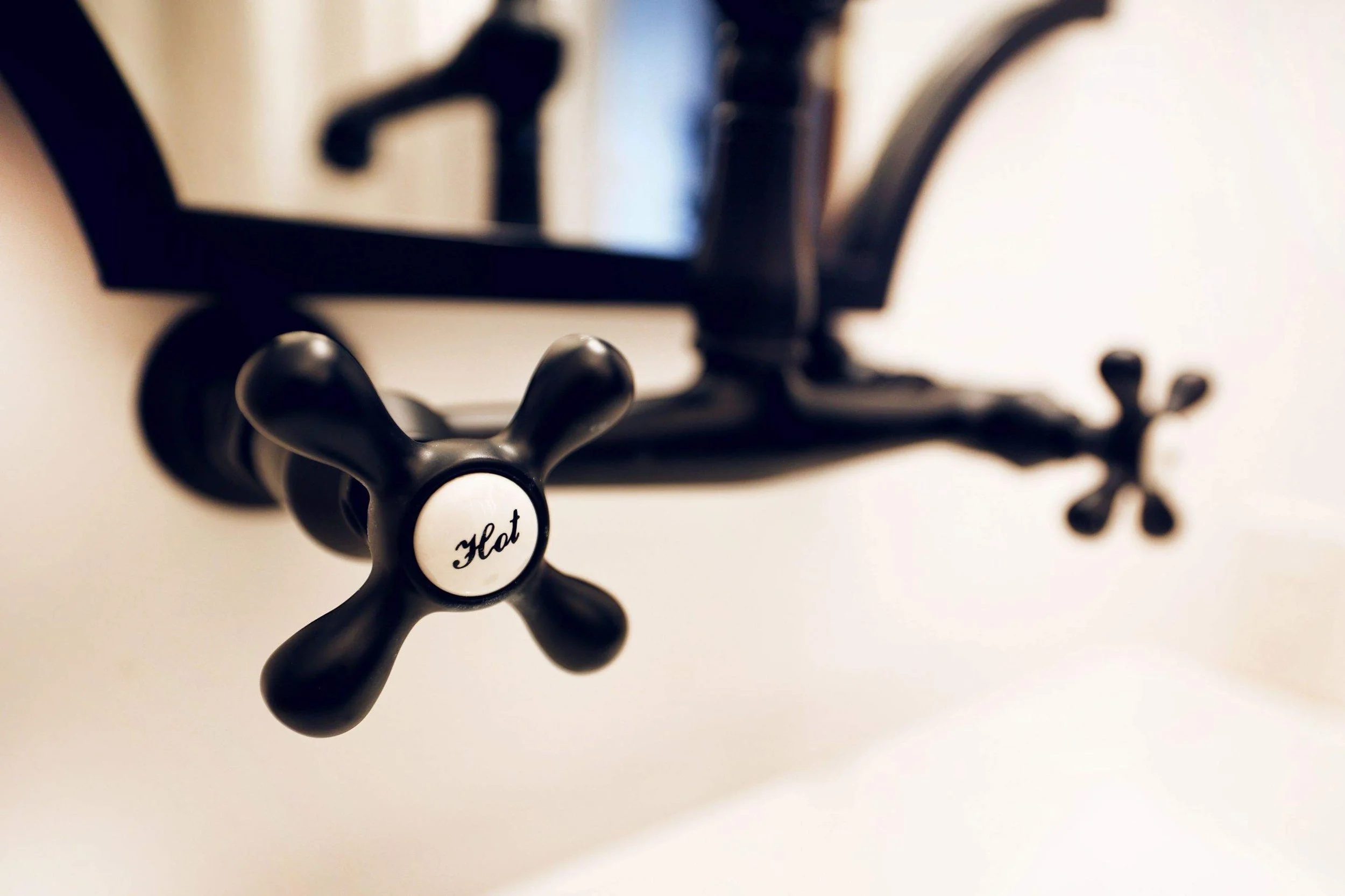 Close-up of a black faucet with a white button labeled 'Hot' in a bathroom.