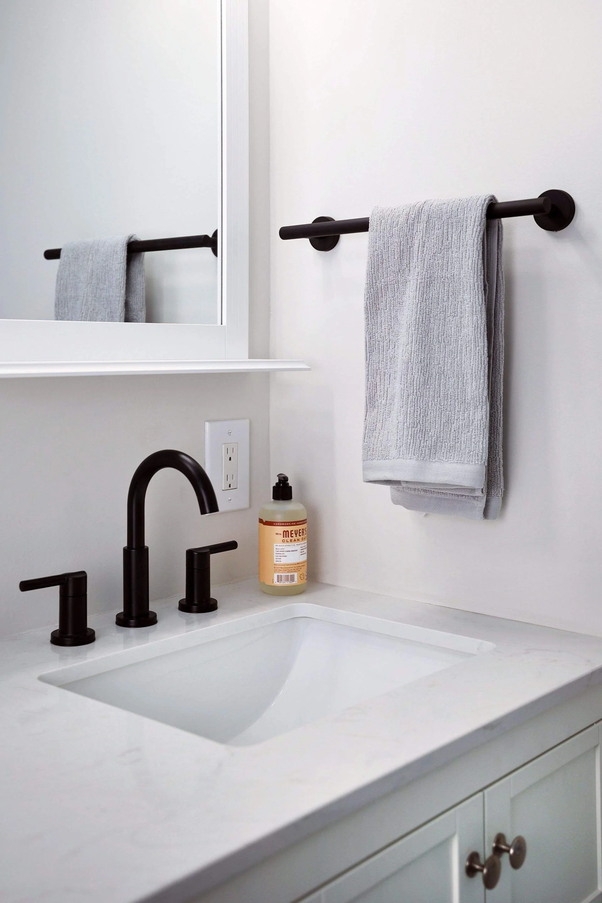 Bathroom sink with black faucet, gray towel on towel bar, and soap dispenser on white countertop.
