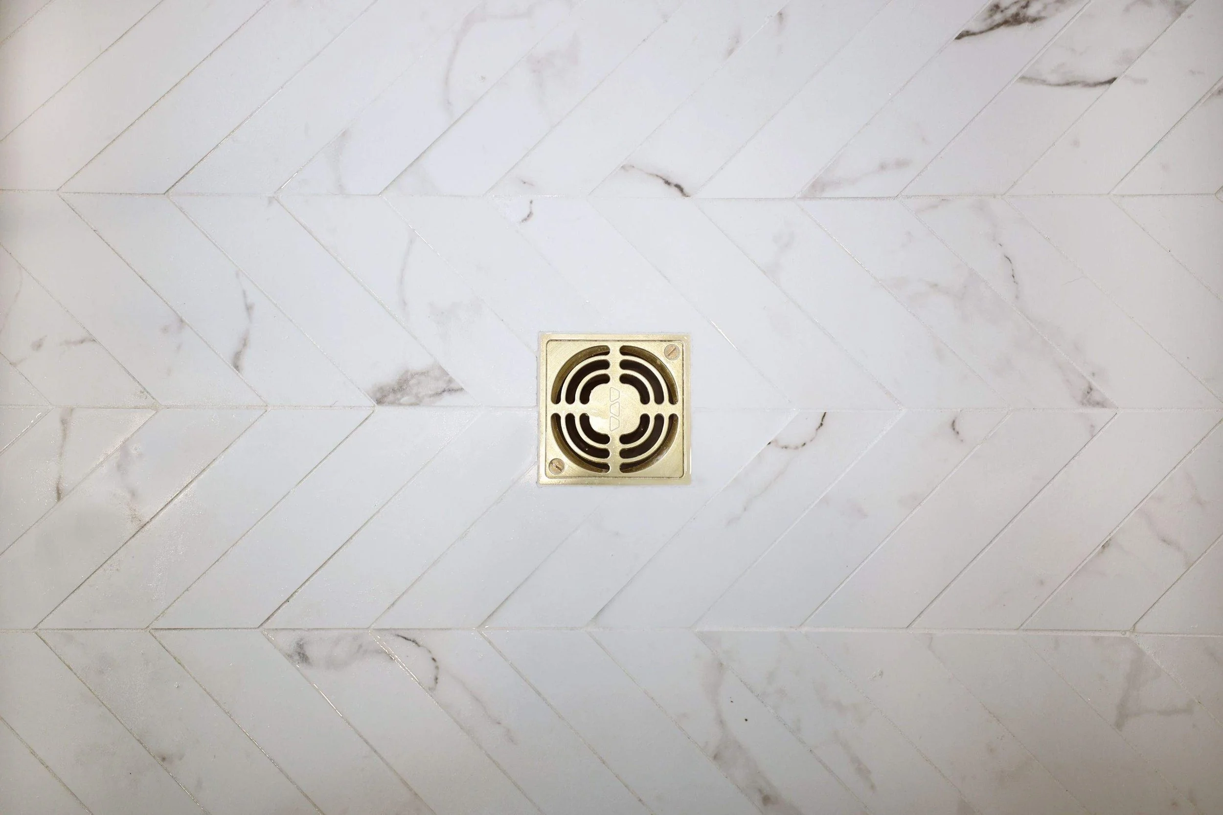 A marble tiled floor with a square drain cover in the center.