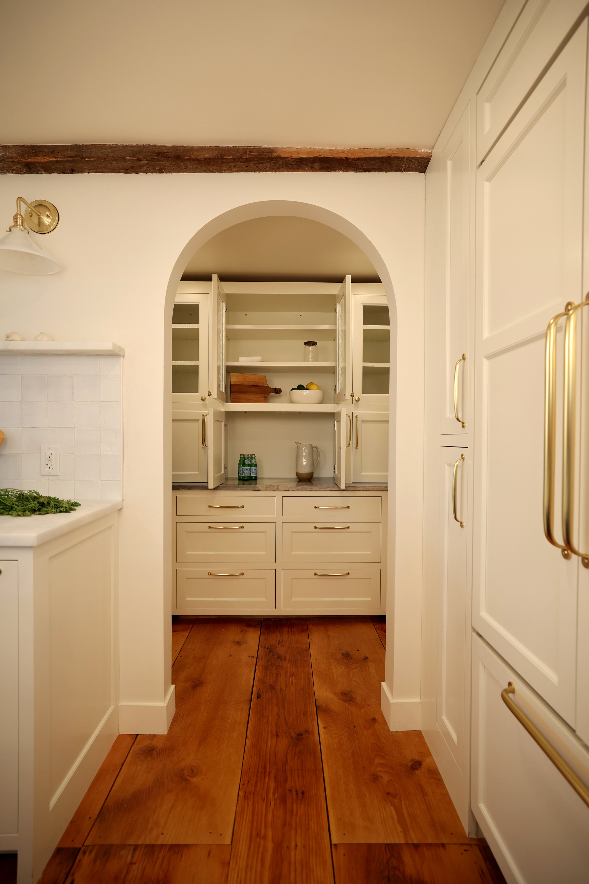  Elegant kitchen featuring a navy-blue island with brass hardware, custom cabinetry, and restored original beams in a historic Upper Valley home. 