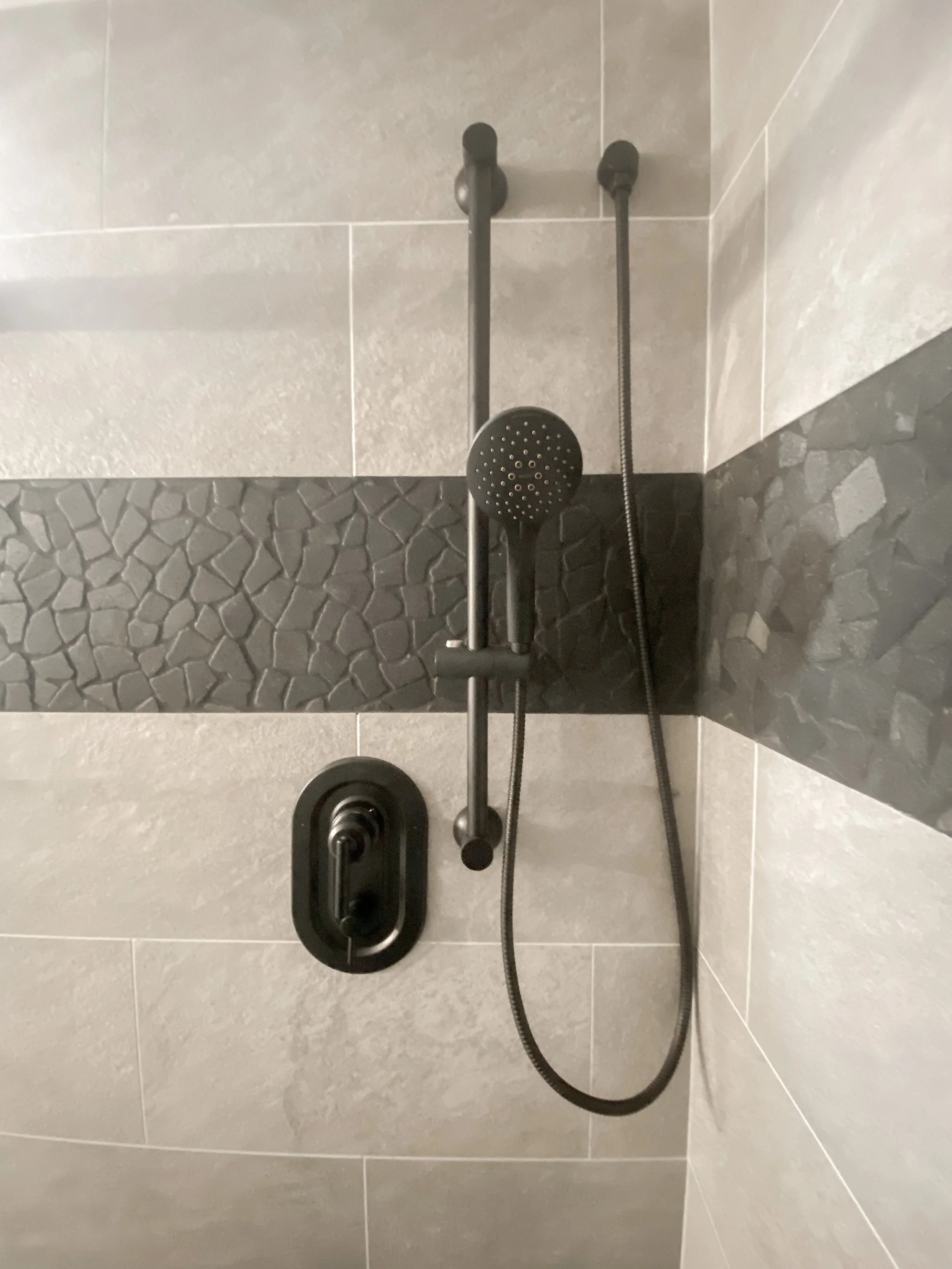 Showerhead and controls in a modern shower with gray and black tiled walls.