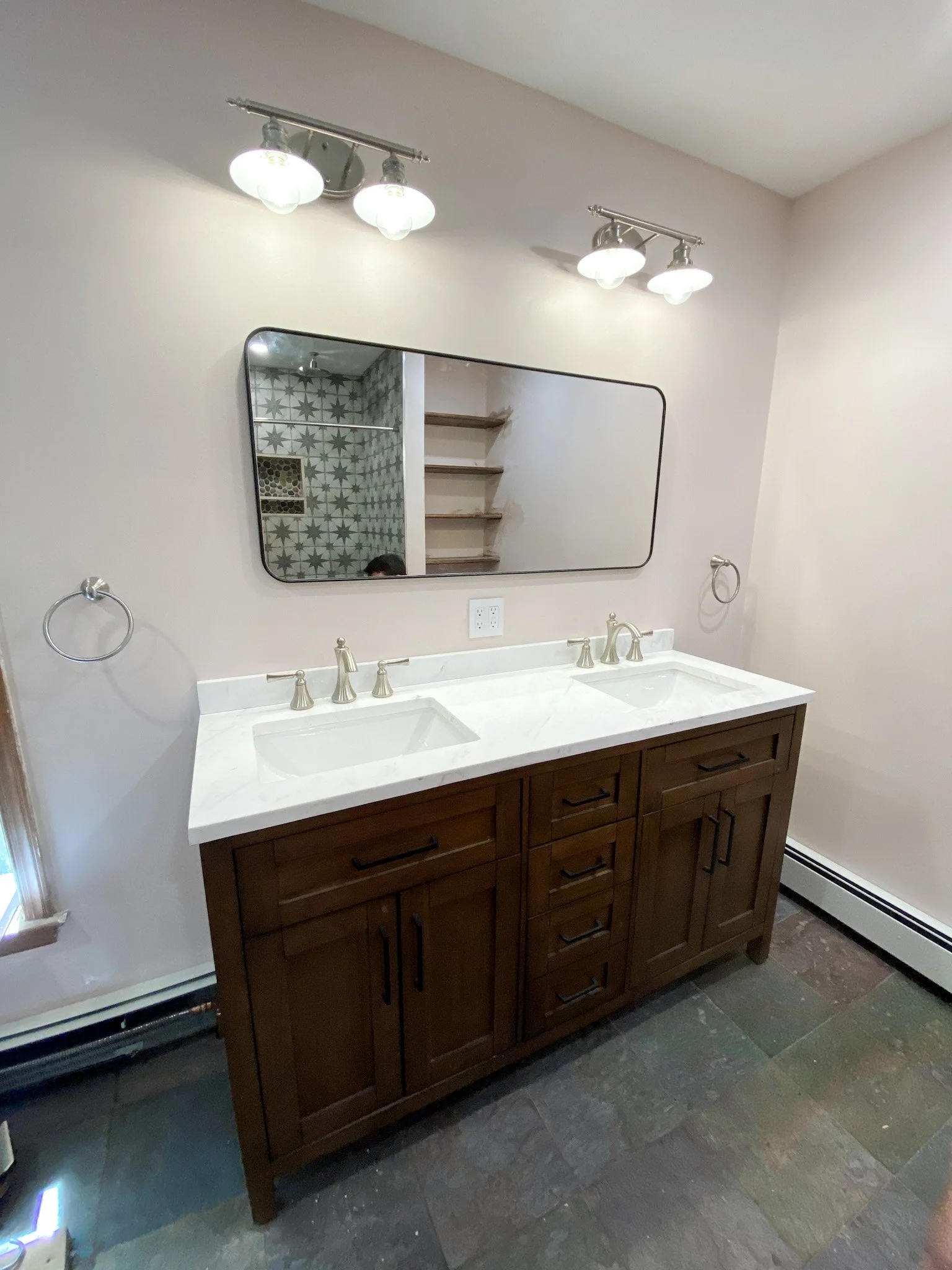 Bathroom vanity with a double sink, wooden cabinet, large mirror, and modern light fixtures above.