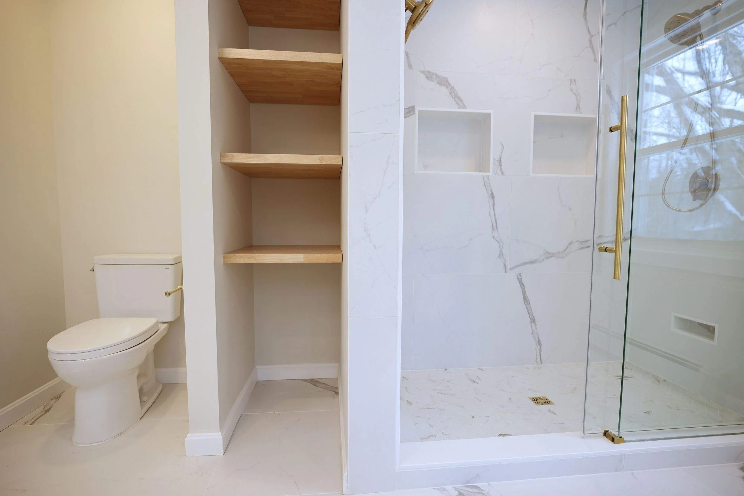 Bathroom with a toilet, wooden shelves, and a glass shower enclosure with marble tiles.