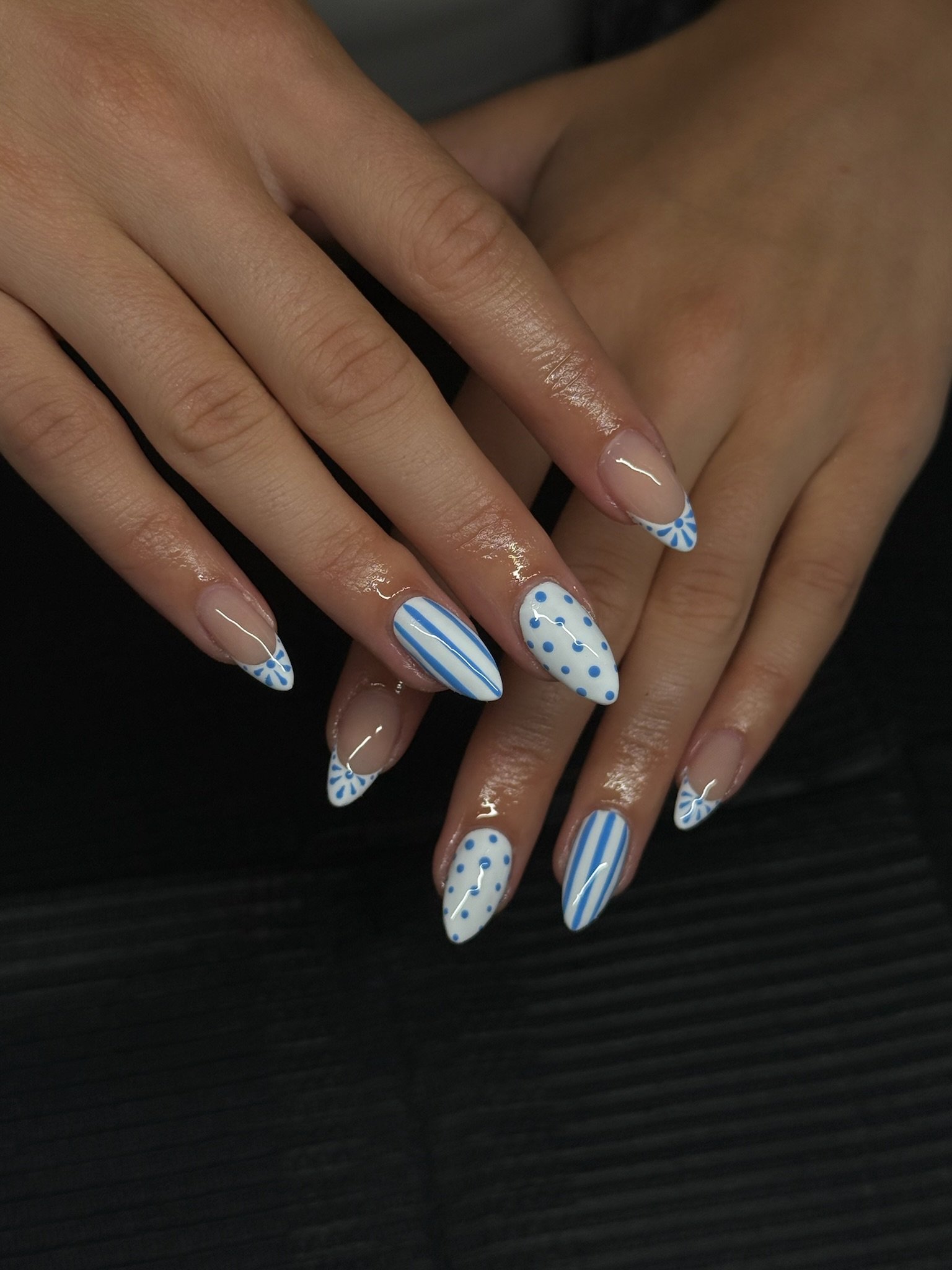 Nail art featuring blue and white striped, dotted, and floral pattern designs on almond-shaped nails.